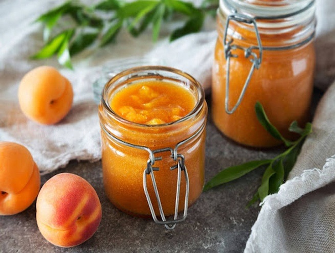 deux pots de confitures au premier plan avec trois abricots posés à côté 