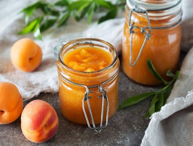 deux pots de confitures au premier plan avec trois abricots posés à côté