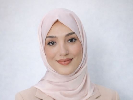 Portrait d’une femme portant un hijab beige et une tenue assortie, regardant l’objectif avec un léger sourire, sur un fond neutre et doux.