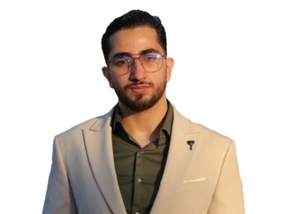 Portrait d’un homme portant des lunettes, une veste beige et une chemise sombre, regardant l’objectif avec une expression sérieuse sur fond clair.