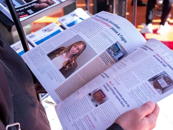 Personne feuilletant un magazine ouvert présentant un article sur l’innovation dans le secteur agroalimentaire, avec la photo portrait d’une femme et plusieurs encadrés illustrés.