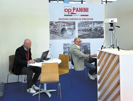 L'image montre deux personnes travaillant au stand de "OP Panini", une entreprise offrant des solutions complètes de stérilisation.