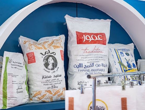 Sacs de farine et de semoule exposés sur une étagère bleue, avec des emballages de produits alimentaires au premier plan.