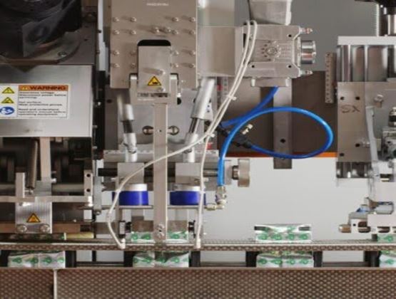 Machine industrielle de conditionnement en fonctionnement, avec des emballages avançant sur une ligne de production automatisée.