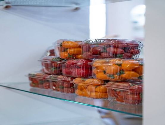 Barquettes transparentes de tomates rouges et orange empilées sur une étagère réfrigérée.
