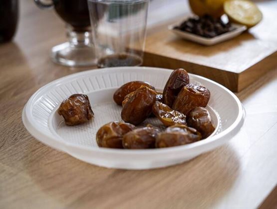 Dattes disposées dans une assiette blanche sur une table en bois.