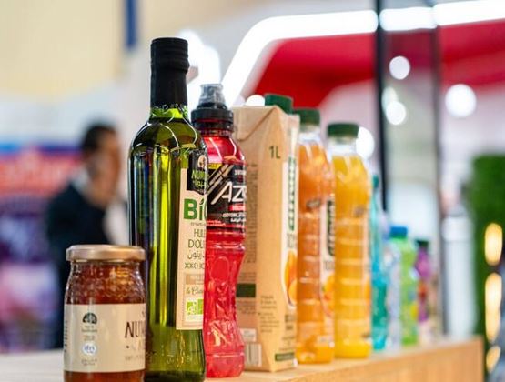 Produits alimentaires et boissons en bouteilles, briques et bocaux exposés sur un présentoir de salon professionnel.