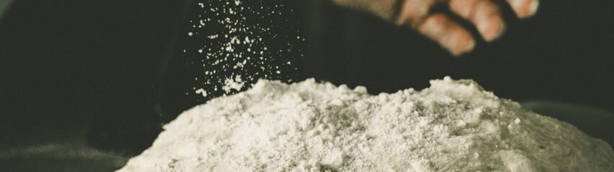 Baker's hand sprinkling flour over bread dough during preparation.