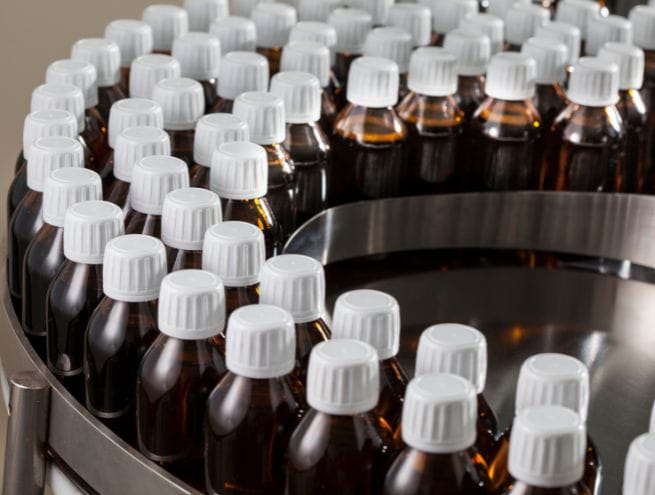 Ligne de production de bouteilles en verre brun avec des bouchons blancs, illustrant l'industrialisation