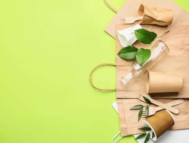 Ensemble d’emballages et d’ustensiles écologiques en papier et bois sur un fond vert.