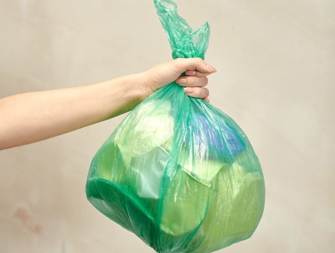 Hand holding a green trash bag filled with waste, symbolizing waste management