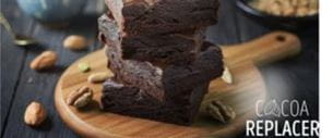 Cocoa-replacer brownies stacked on a wooden board, topped with nuts.