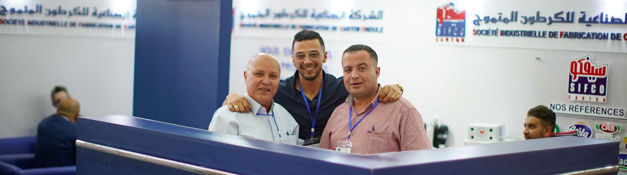 Trois hommes souriant derrière un stand