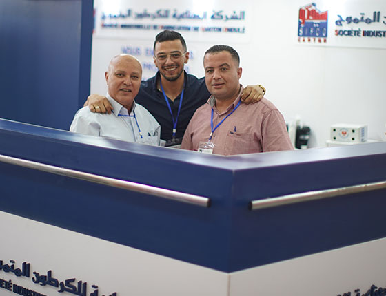 Three men smiling behind a stand